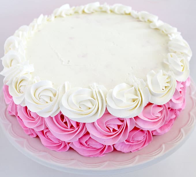 Finally, use the white cream to pipe the third row of roses around the sides and the entire top of the cake.