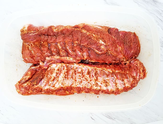 To marinate the ribs with your homemade spice rub, place the racks into a large rectangular Tupperware container. 