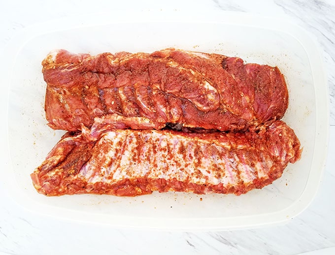 To marinate the ribs with your homemade spice rub, place the racks into a large rectangular Tupperware container.