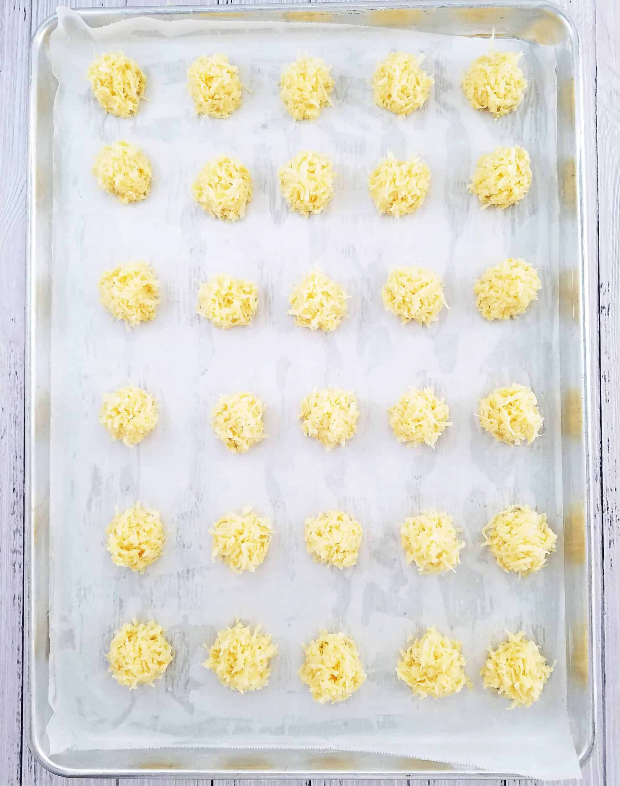 Time to prep the cookies for baking! We’ll scoop the coconut mixture and place it onto a baking sheet lined with parchment paper. Shape the bottom of each cookie into a circular shape.