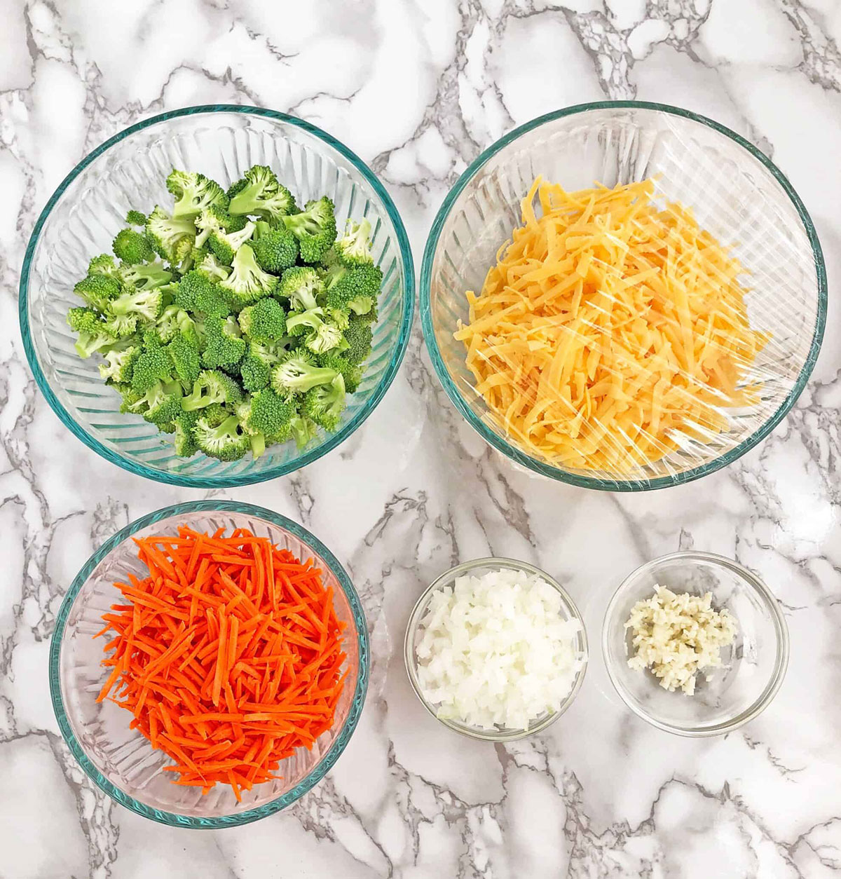 Cut the broccoli into florets that are about bite-sized pieces, grate the carrots, and shred the cheese. Place them all in bowls and cover them all with plastic wrap. 