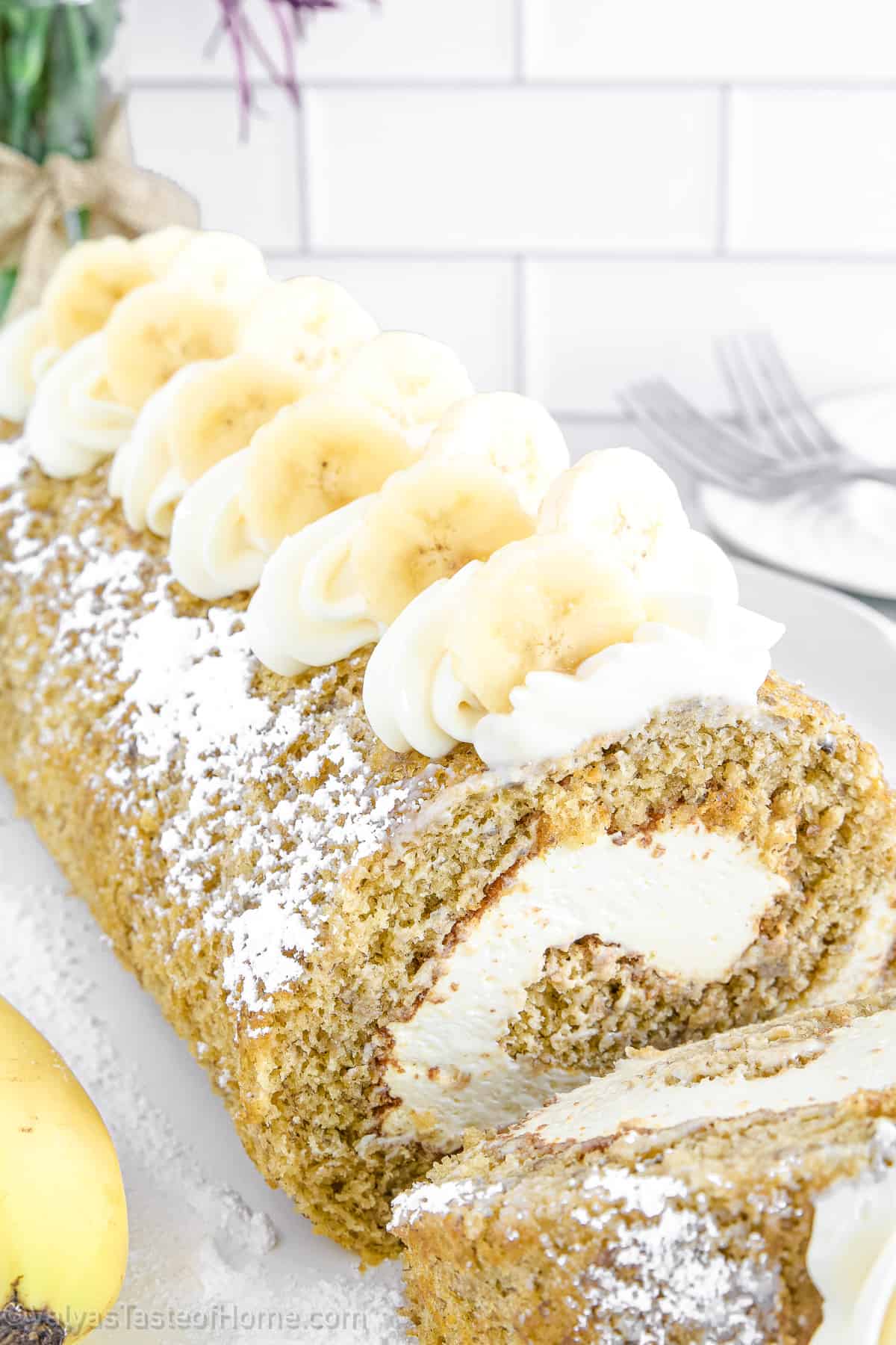 This Banana Roll recipe features a fluffy and moist banana sponge cake filled with creamy and rich cream cheese frosting. It's then rolled up into a spiral shape and dusted with powdered sugar.