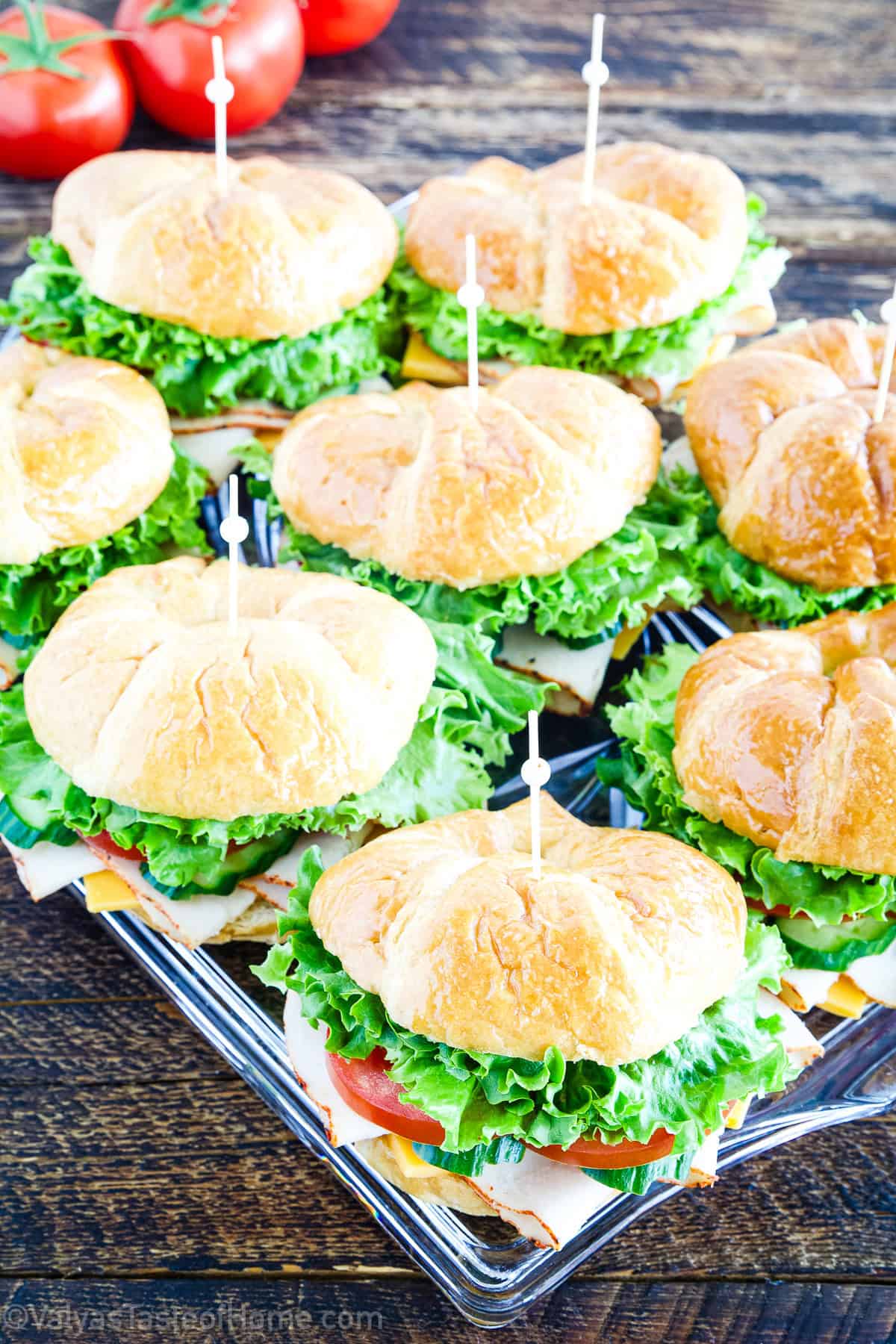 Overhead shot of turkey croissant sandwiches with lettuce, tomato, cucumber, turkey, and cheese on a white plate.