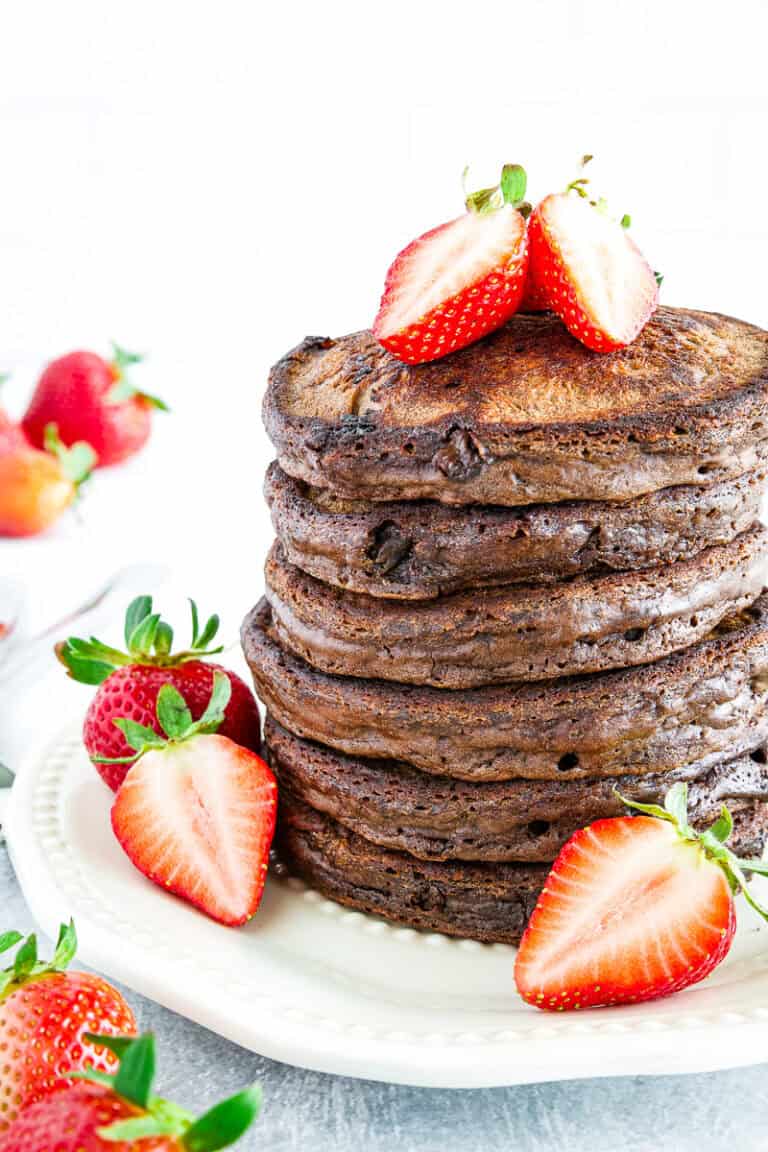 A stack of sourdough discard chocolate pancakes topped and surrounded by fresh, halved strawberries on a white plate.